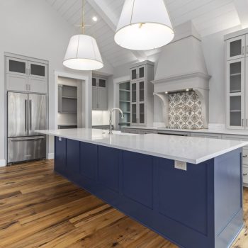 Modern kitchen with a blue island, white countertops, stainless steel appliances, and wood flooring.