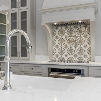 Modern kitchen with a marble island, stainless steel faucet, and patterned tile backsplash above the stove.