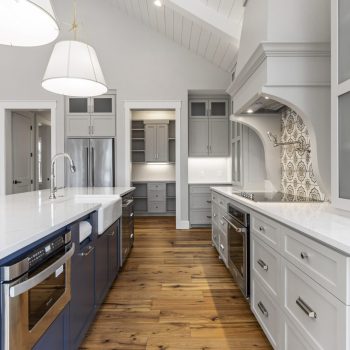 Modern kitchen with white countertops, blue island, stainless steel appliances, and wooden flooring.