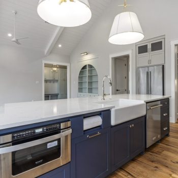 Modern kitchen with a large island, blue lower cabinets, built-in appliances, and wood flooring.