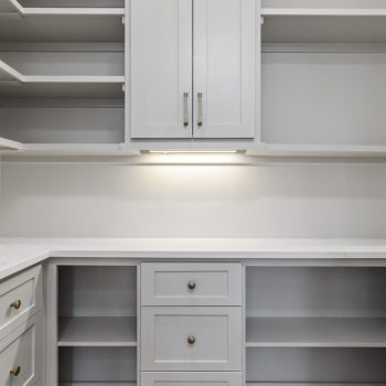 Modern pantry with gray cabinets, drawers, shelves, and under-cabinet lighting against a white wall.