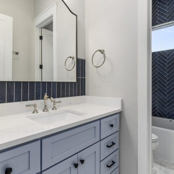 Modern bathroom with a white vanity, rectangular sink, wall mirror, and a shower with dark blue herringbone tile.