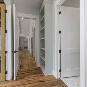Interior hallway with wooden floors, open doors, built-in shelves, and a door with textured glass panel on the left.