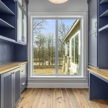 Narrow room with blue cabinets, wood counters, and a large window overlooking a yard with bare trees.