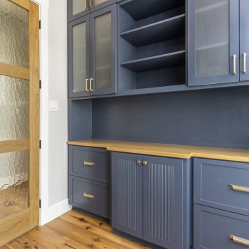 Built-in blue cabinetry with gold handles and wooden countertop next to a wooden door with frosted glass panels.