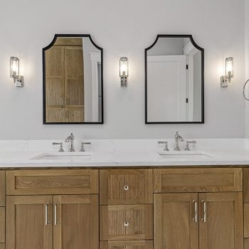 Double bathroom vanity with wooden cabinets, two sinks, two mirrors, and wall-mounted lights on a light gray wall.