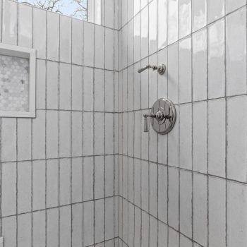Shower with vertical white subway tile, built-in niche, chrome fixtures, and a window showing a blue sky.