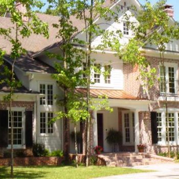 Two-story brick and white siding house with large windows, black shutters, and a covered front porch with plants.
