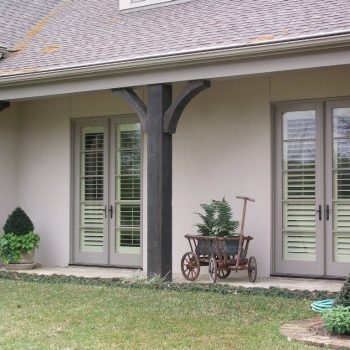Covered patio with double French doors, two potted plants, a small shrub, and a decorative vintage cart with ferns.