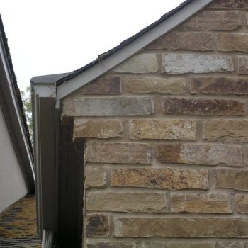 Close-up view of a brick wall and roof edge with a narrow gap between two houses.