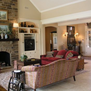 A traditional living room with patterned sofas, a fireplace, built-in shelves, and a view into an adjoining room.