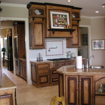 Spacious kitchen with wooden cabinets, granite countertops, a gas stove, and decorative artwork above the range.