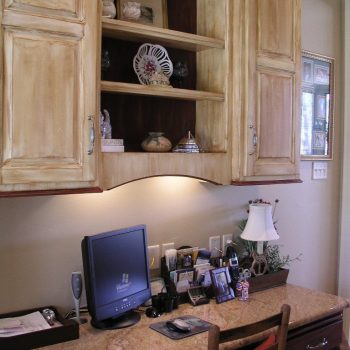 Home office workspace with a desktop computer, lamp, chair, and shelves displaying decorative items above the desk.