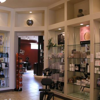 Modern hair salon interior with glass shelves displaying hair products and posters on the walls.