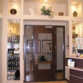 Reception area with glass door, shelves of products, decorative vases, and tile flooring under bright lighting.