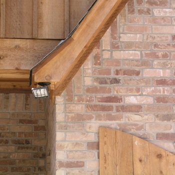 Close-up of a brick and wood exterior wall with a small outdoor light fixture mounted under the roof eave.