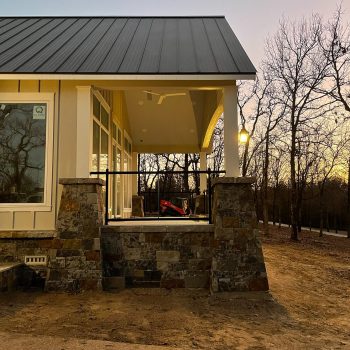 Modern house with large windows and stone accents, set against leafless trees at dusk.