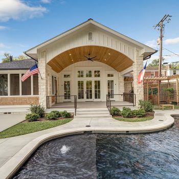 Modern house with large windows, a curved patio roof, two flags, and a swimming pool in the foreground.