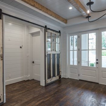 Room with dark wood floors, white shiplap walls, exposed ceiling beams, sliding barn doors, and glass double doors.