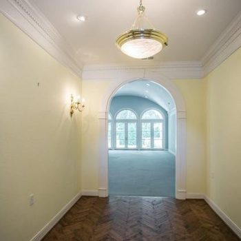 Hallway with yellow walls, wood herringbone floor, and arched entry leading to a bright room with large windows.