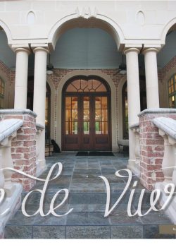 Brick and stone entryway with arched columns, glass doors, and "Joie de Vivre" text overlay at the bottom.
