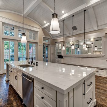 Spacious modern kitchen with white cabinets, marble island, pendant lights, and large windows overlooking a patio.