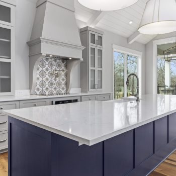 Modern kitchen with a large navy island, white marble countertop, and stainless steel appliances, featuring ample natural light.