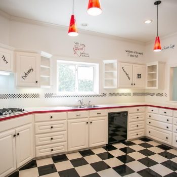 White kitchen with black and white checkered floor, red pendant lights, and words painted on the walls above cabinets.