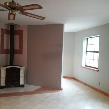 Unfurnished room with a ceiling fan, wood stove in the corner, tiled wall, and a window with natural light.