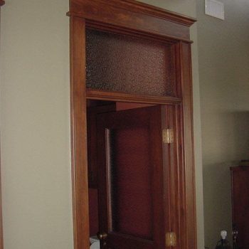 A wooden door with a textured glass transom window above, set in a beige wall with wood trim.