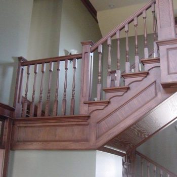 Wooden staircase with decorative balusters and railings inside a house, viewed from below at an upward angle.