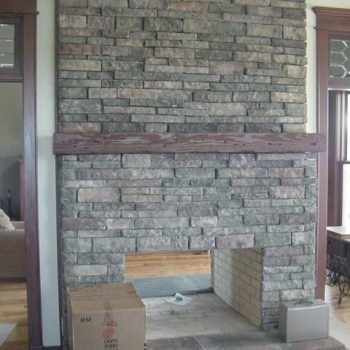 Stone fireplace with a double-sided firebox, wooden mantel, and a cardboard box on the hearth.