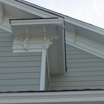Close-up of a house's gable roof with decorative brackets and light gray horizontal siding.