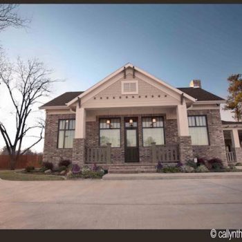 Single-story house with large windows, stone exterior, and front porch, photographed at sunset.