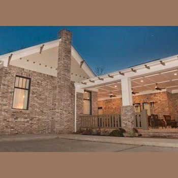 Single-story brick house with large covered porch, outdoor seating, and exterior lights on at dusk.