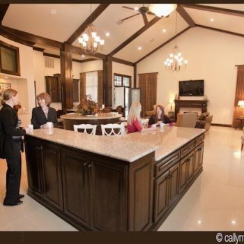 Four women converse around a large kitchen island in a spacious, modern open-concept living area.