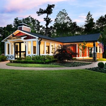Single-story house with a covered porch, manicured lawn, and surrounding trees at dusk.