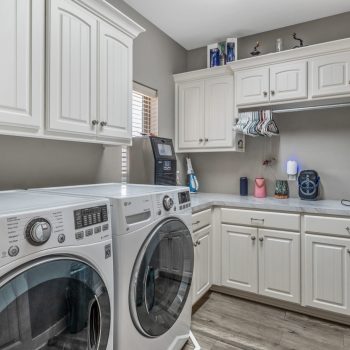 Laundry room with white cabinets, front-loading washer and dryer, countertop, and cleaning supplies on the counter.
