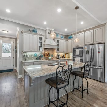 Modern kitchen with gray cabinets, stainless steel appliances, island with marble countertop, and two barstools.