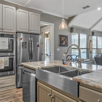 Modern kitchen with stainless steel appliances, double sink, marble countertops, and open view to living room.